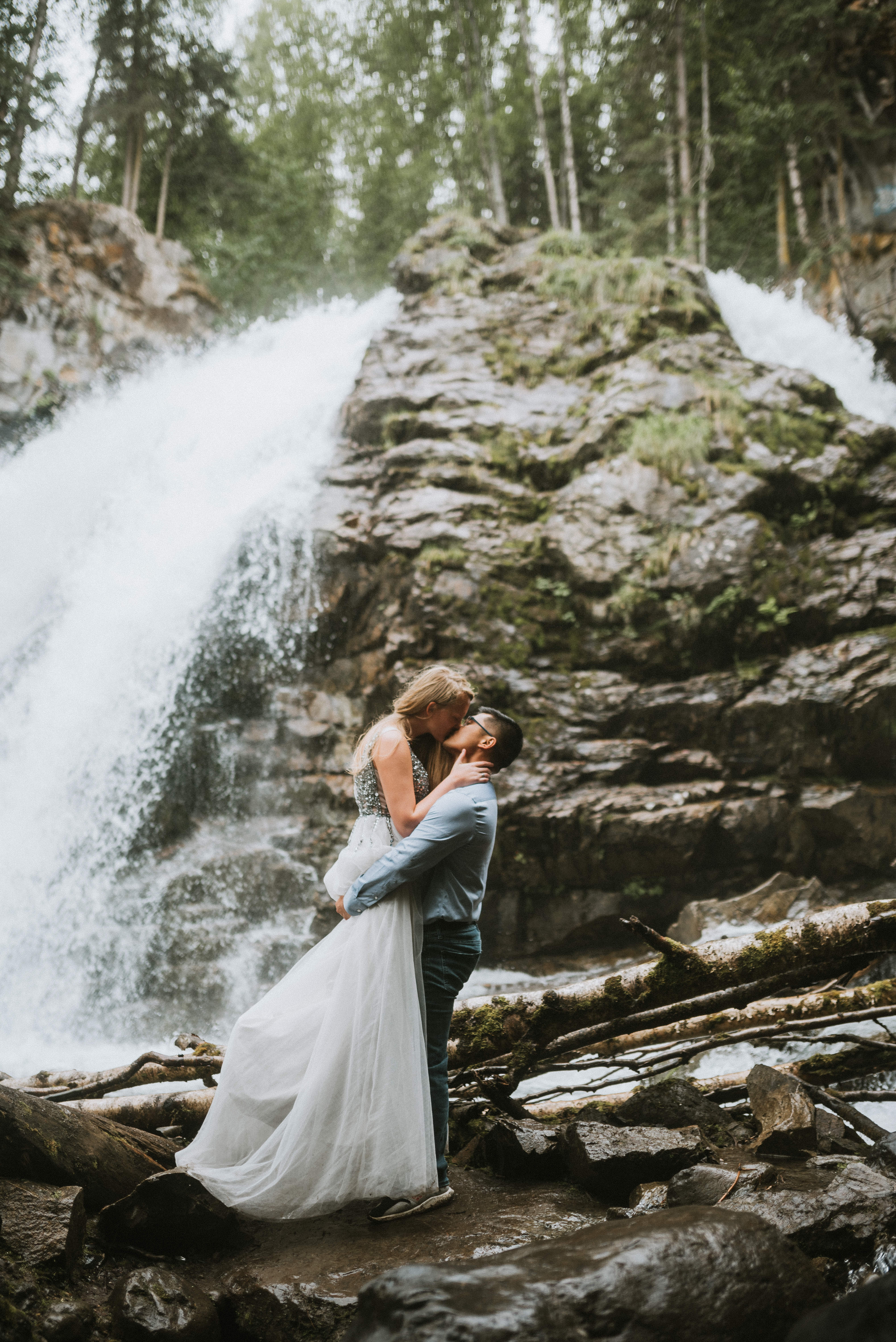 Couple dressed up and kissing in front of Barbara Falls during their Engagement Photos in Alaska