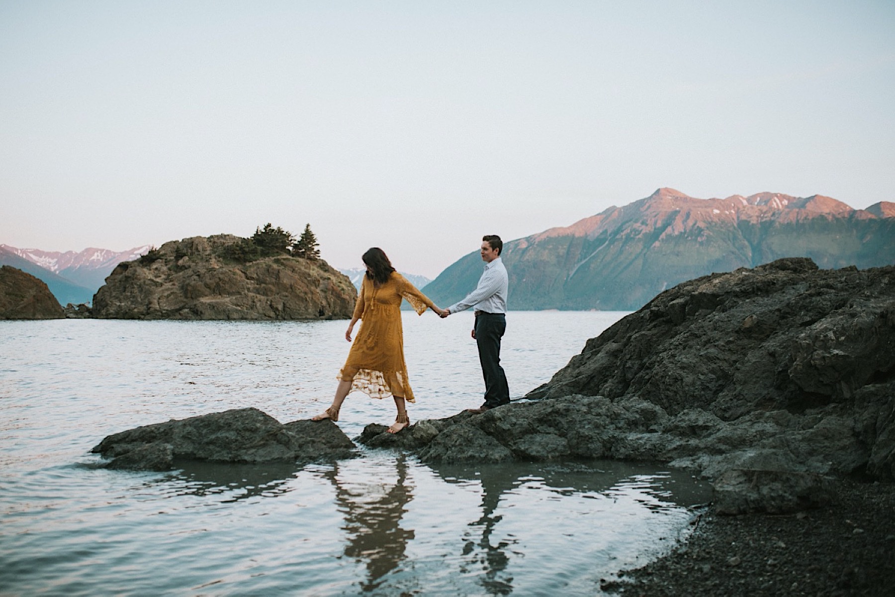 Couple standing on rocks, she is leading him out by the water