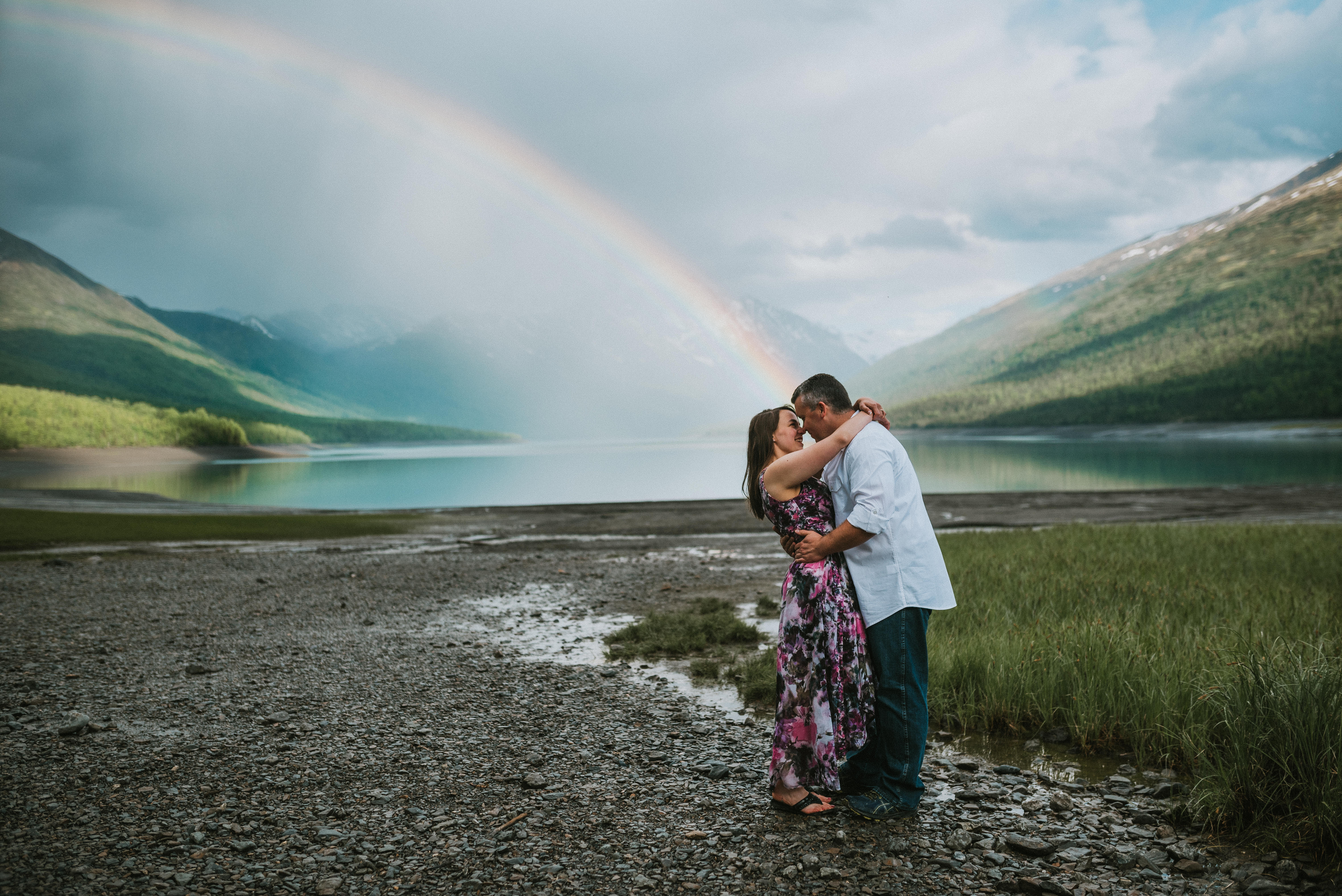 Couple kissing at the end of a rainbow at Eklutna Lake Alaska during their Engagement photos