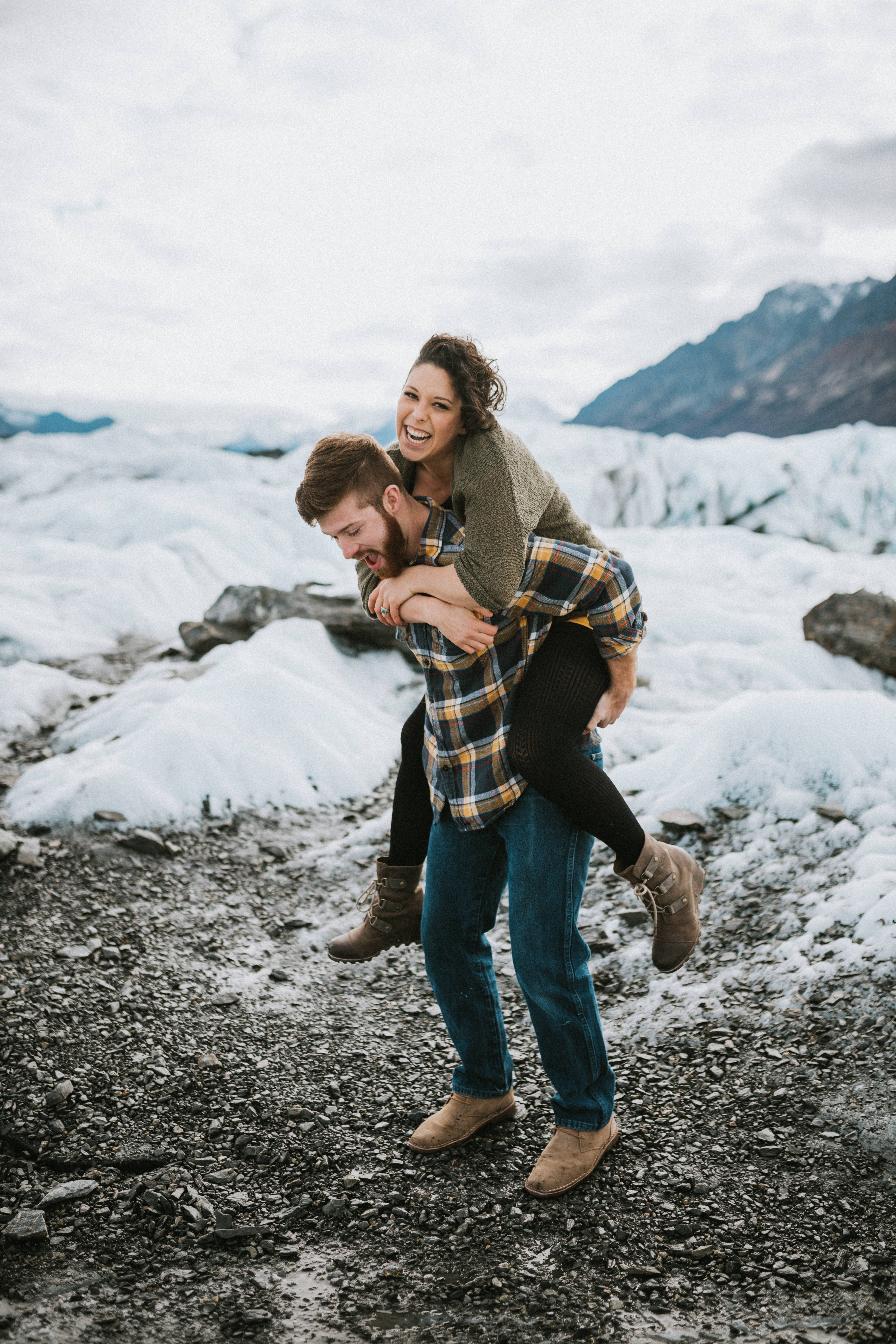 An engaged couple piggy backing at Matanuska Glacier during engagement session in Alaska