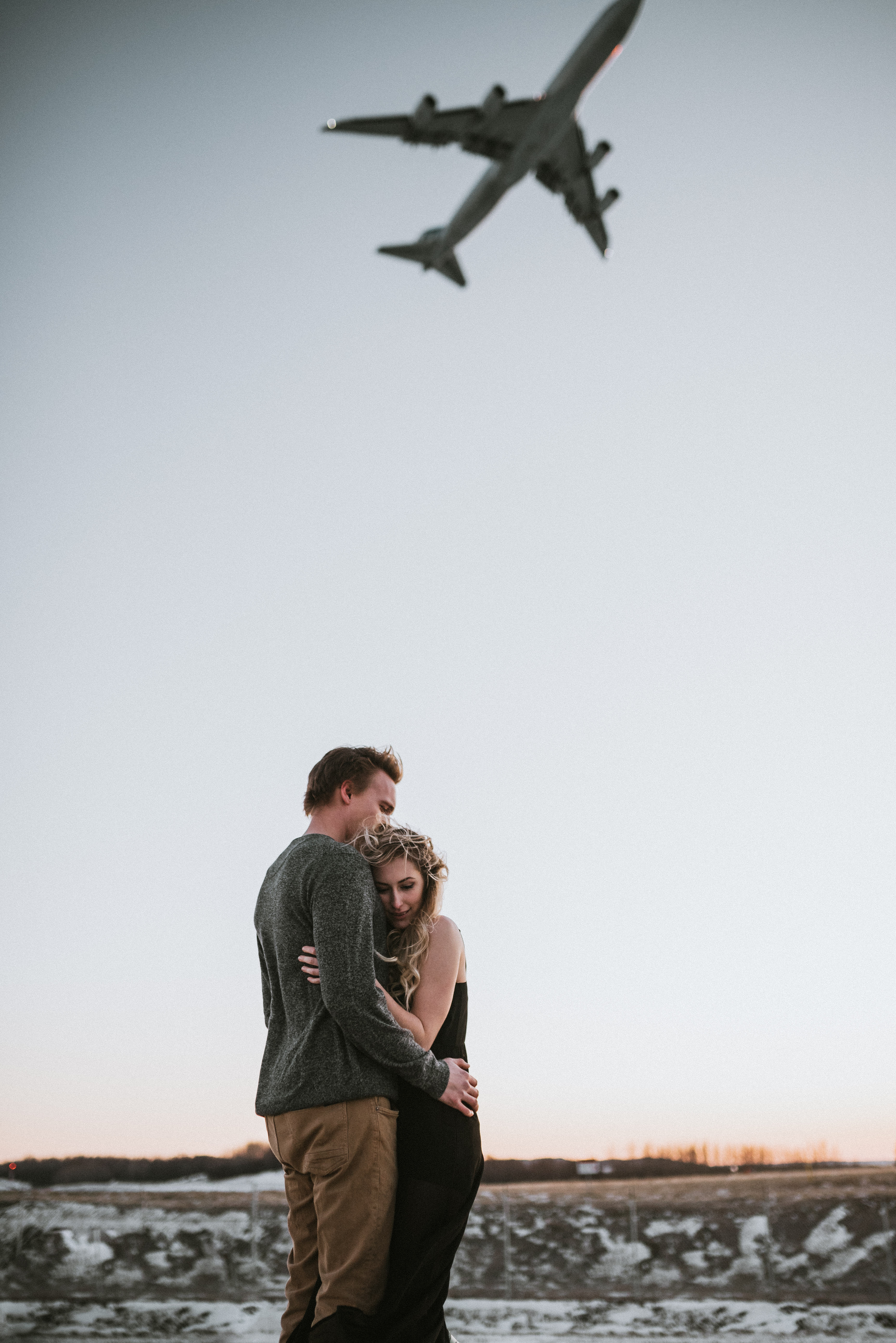 Alaska Engagement Photos, couple hugging under an airplane as it flies over in the winter