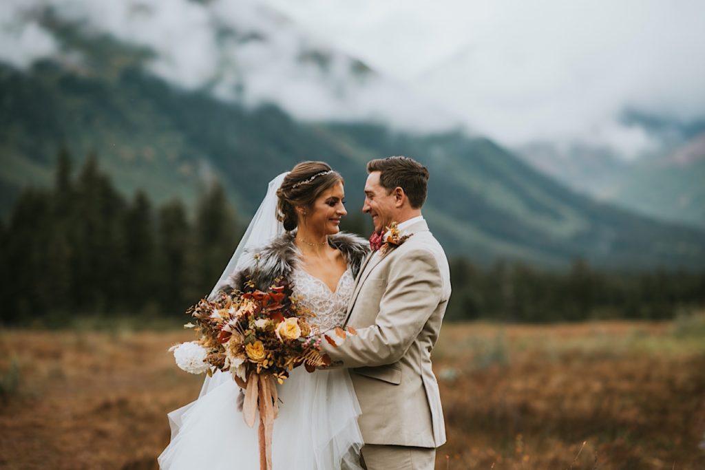 Bride and groom smiling at each other in front of a Girdwood mountain backdrop
