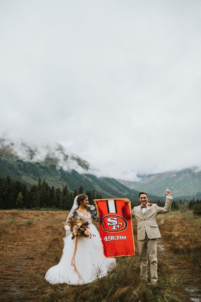 Bride and groom who are 49ers fans holding a red and gold flag up on their wedding day