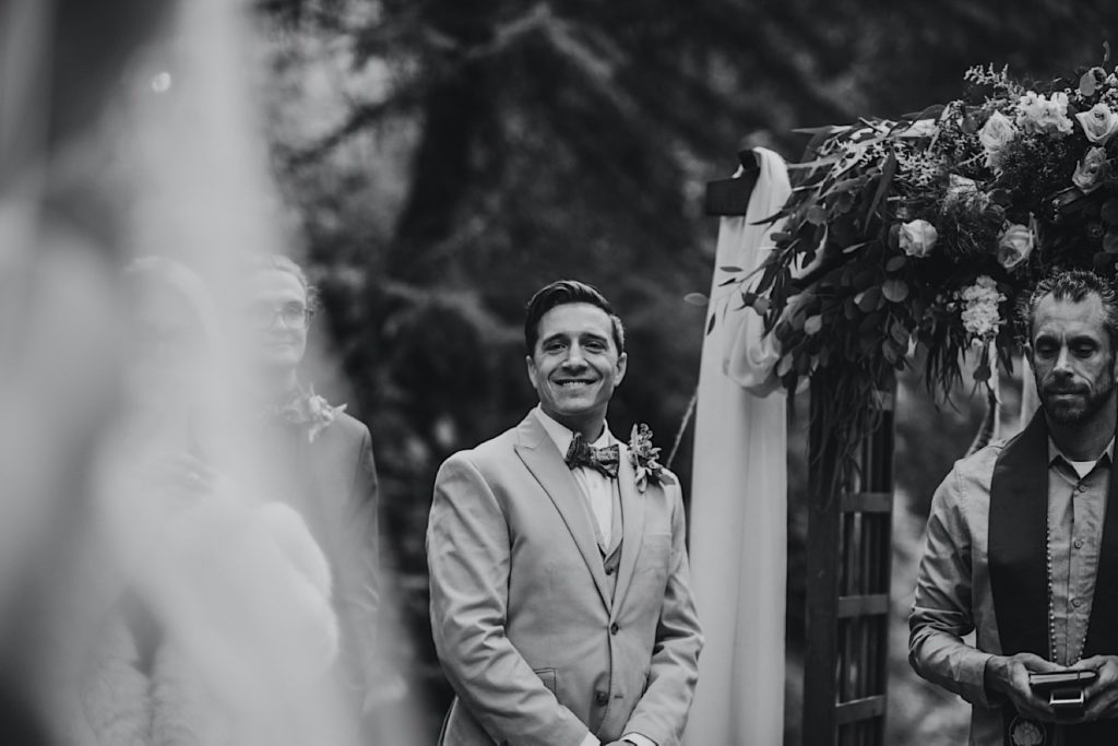 Black and white photo of the groom seeing his bride walk down the path at Raven Glacier Lodge