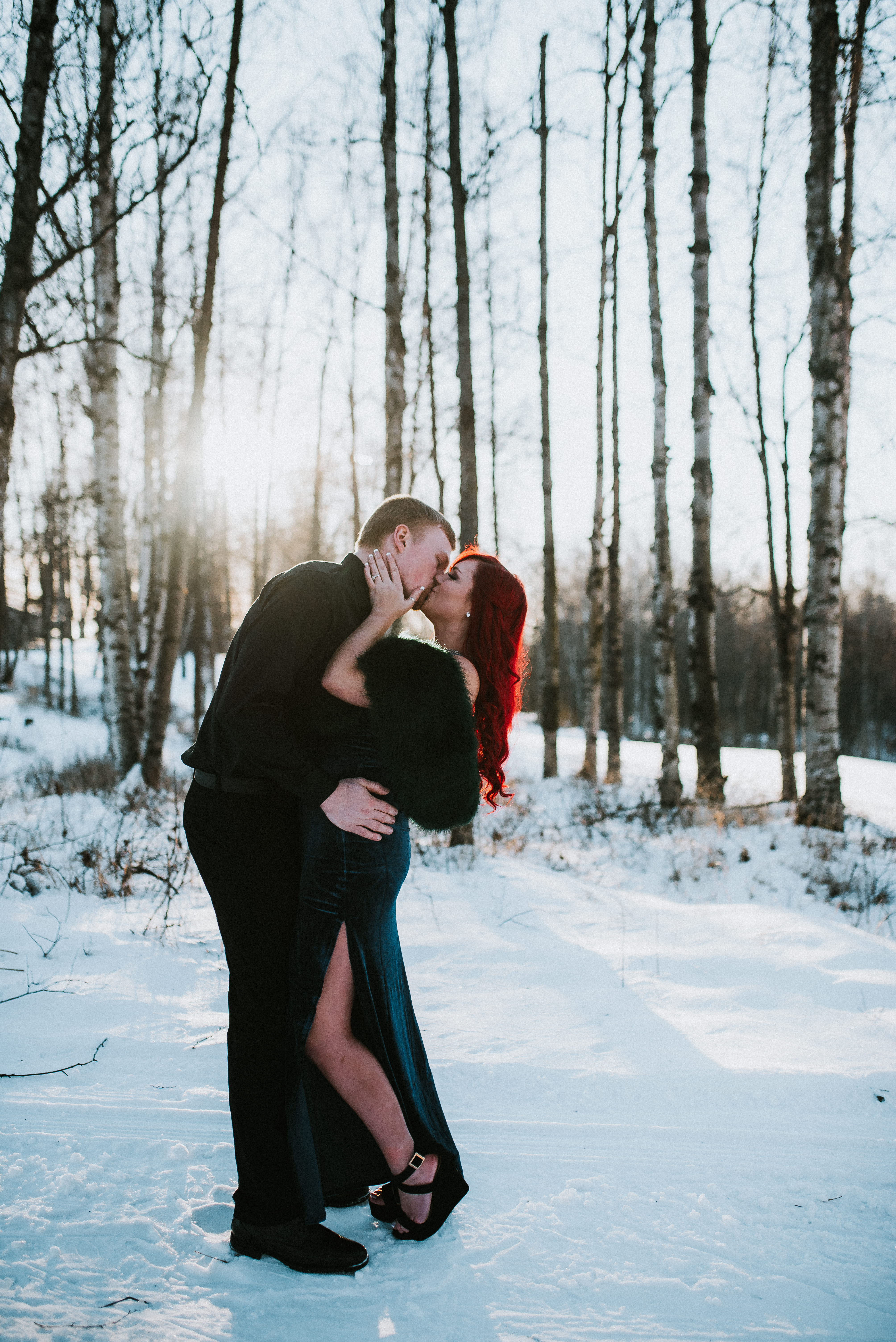 Couple dip kissing in fancy outfits in the snow and winter light at Russian Jack Springs Park