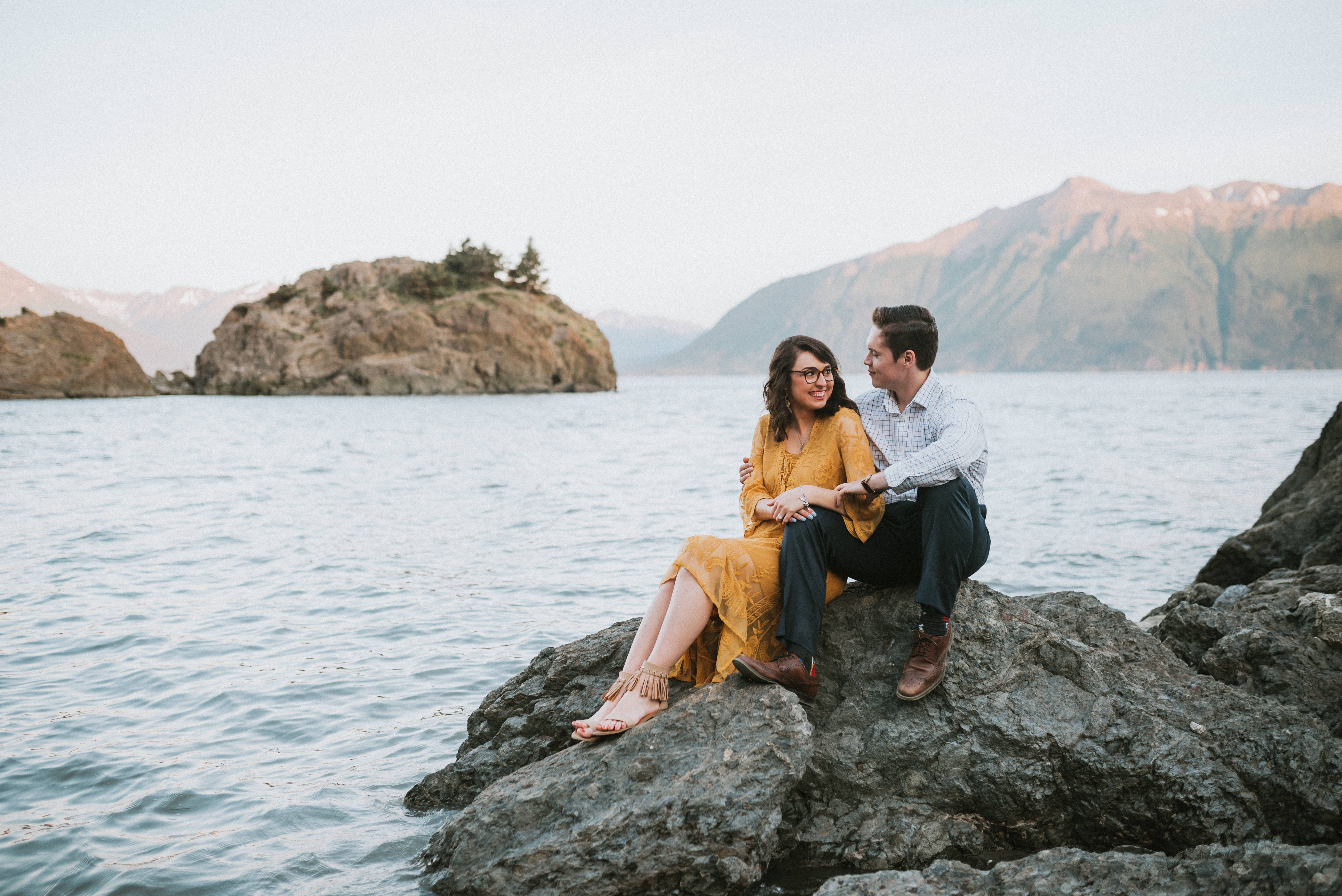 Couple sitting on rock formation by the water at Beluga Point during engagement photos in Alaska 