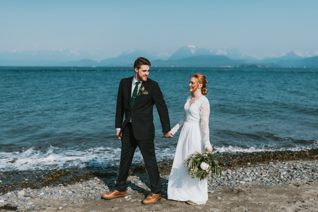 Groom leading his bride down the beach in Homer after their elopement