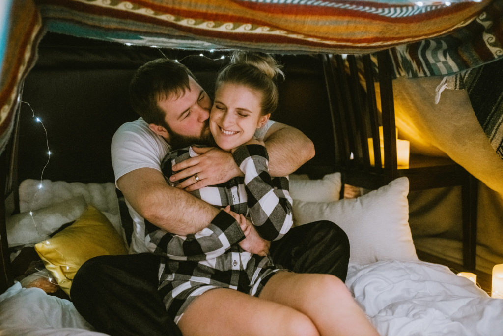 Couple snuggling and smiling in a candle lit blanket fort during a date night