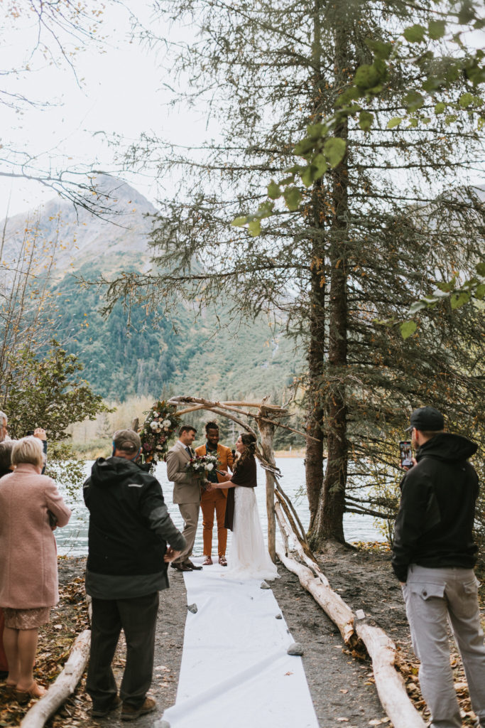 Lakeside ceremony with floral arch against a mountain and glacier backdrop