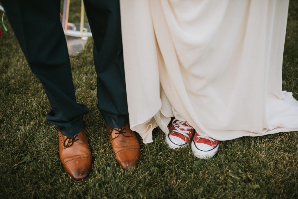 Bride and groom showing their wedding shoes off, brown leather shoes and red converse