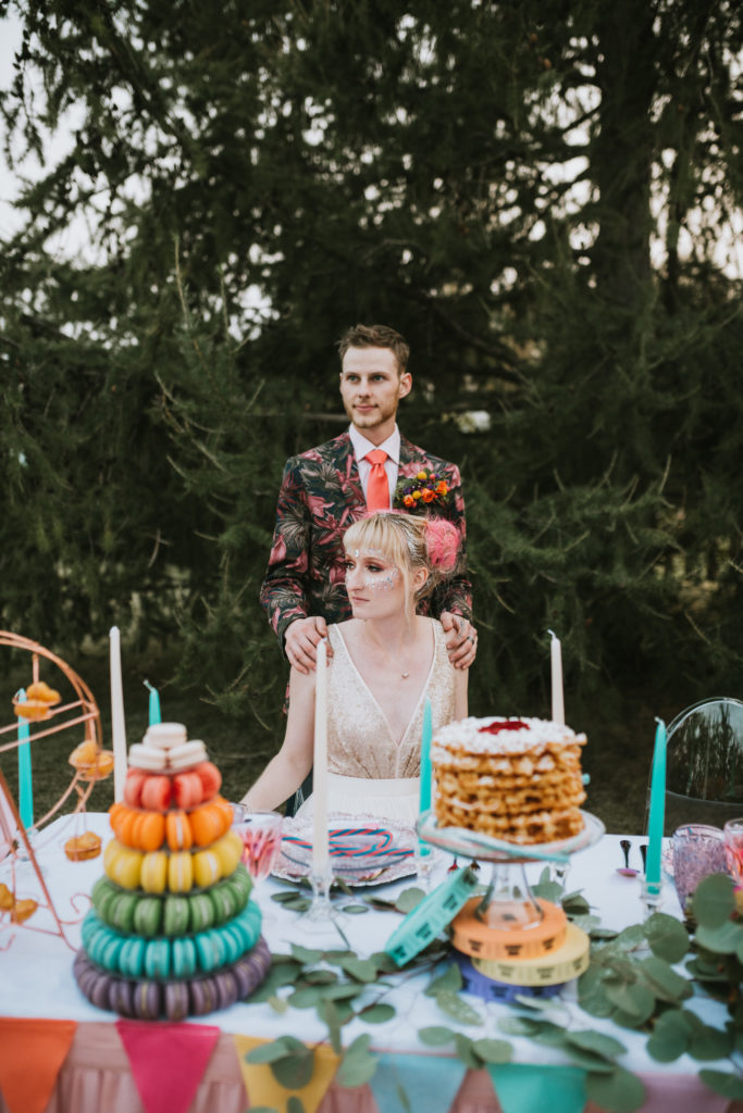 Bride and groom standing behind their carnival theme colorful dessert table at the alaska state fair