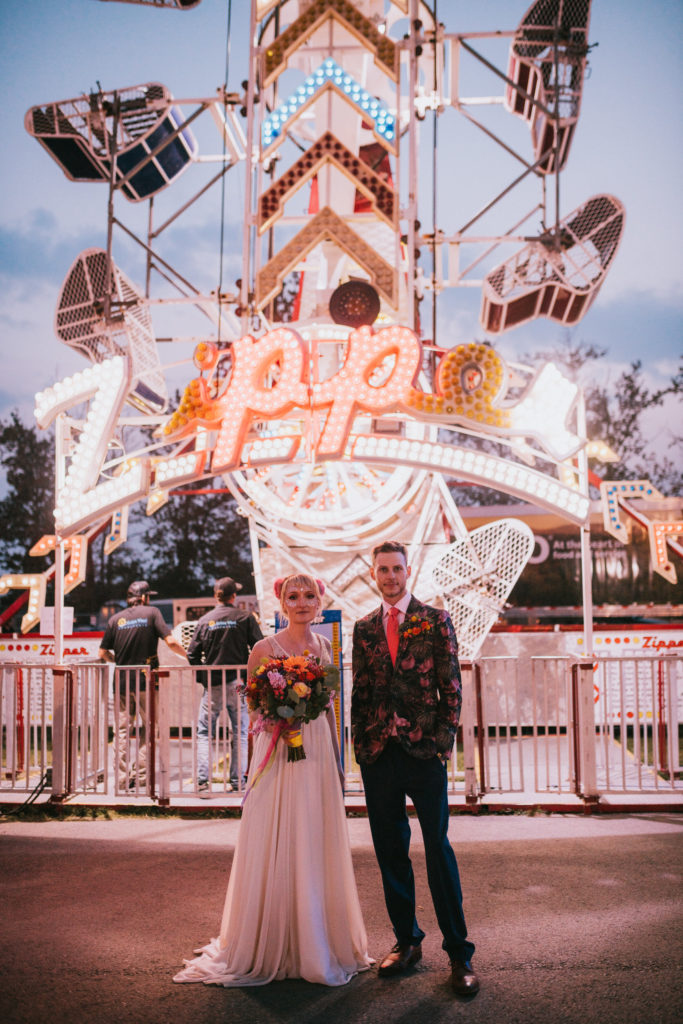 Bride and groom standing in front of a neon state fair ride