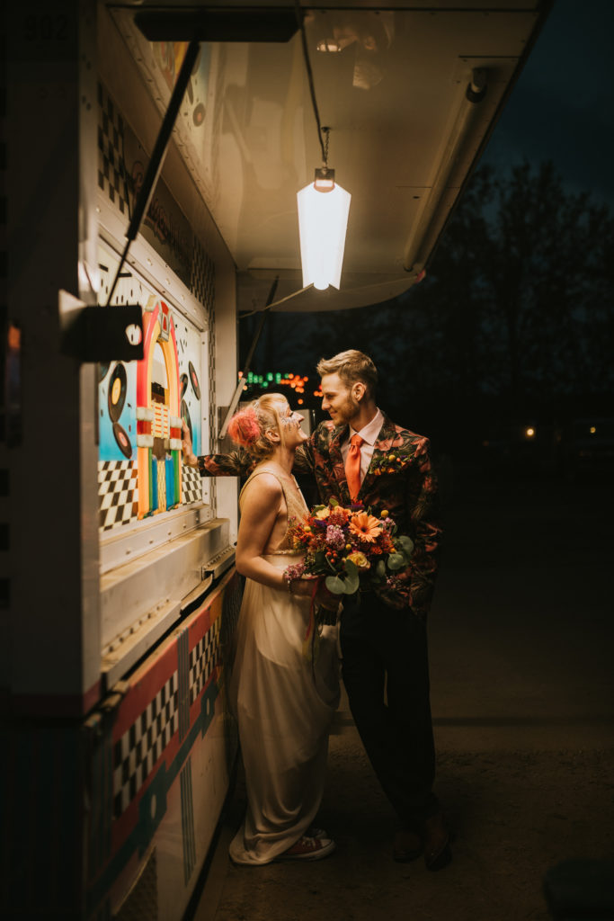 Bride and groom leaning against fair booth in fluorescent light