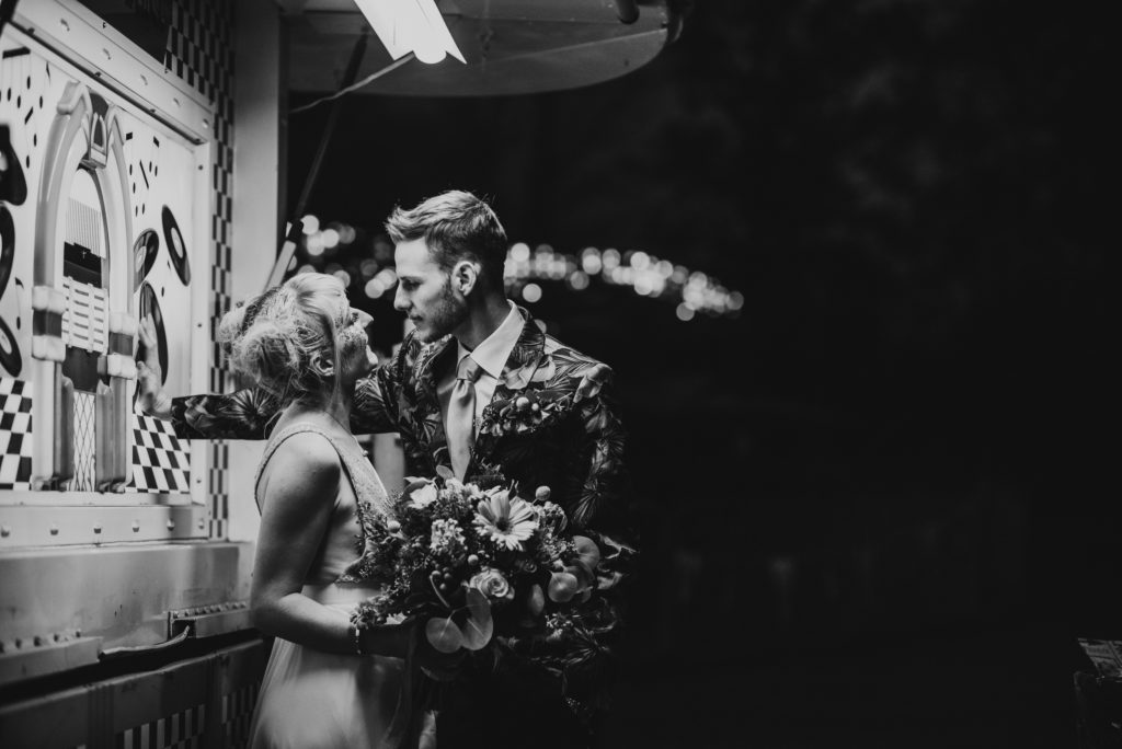 black and white photo of bride and groom smiling at each other under neon lights
