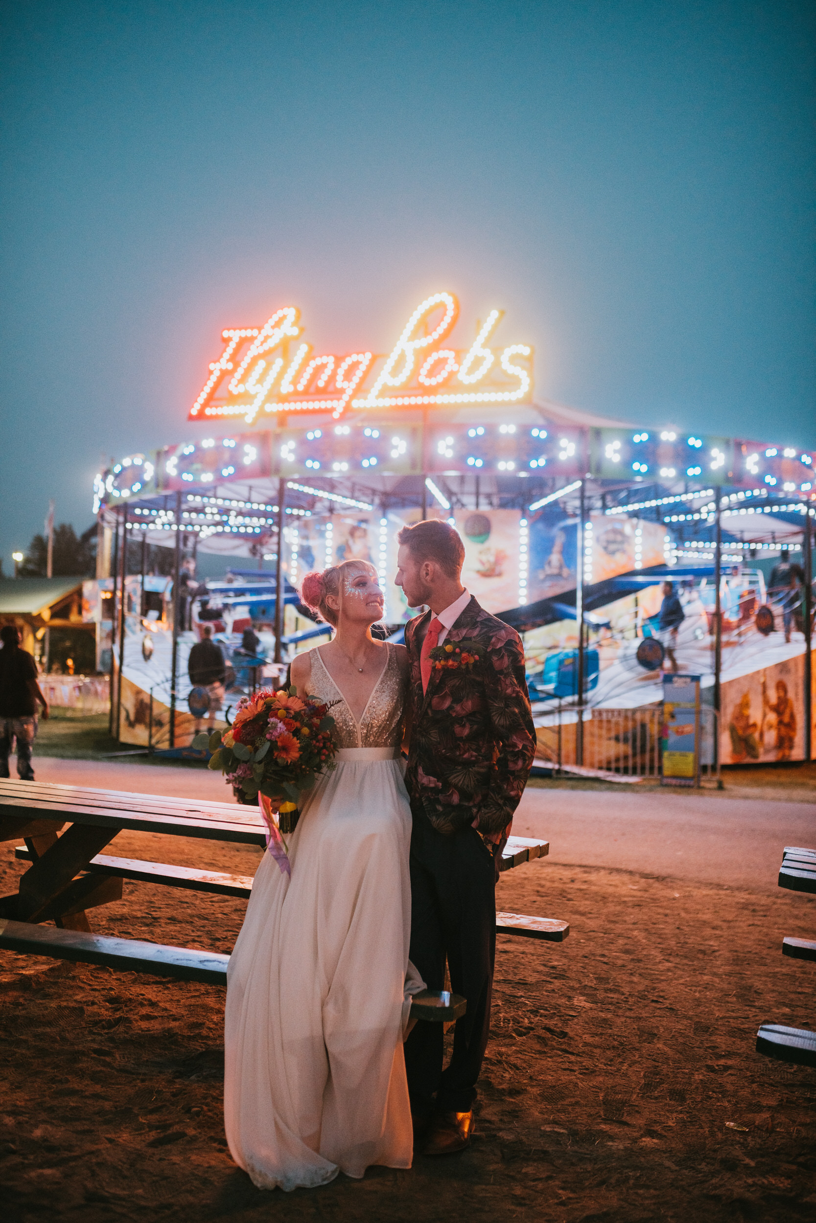 Colorful bride and groom in front of flying bobs neon signs at the alaska state fair