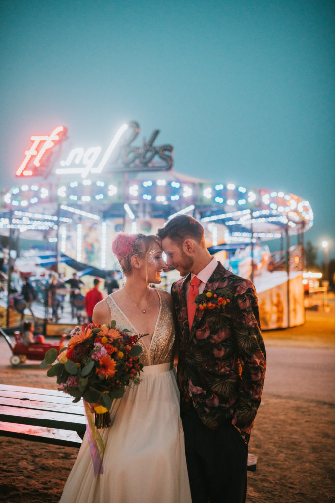Bride and groom nuzzling their faces together in front of a alaska state fair ride