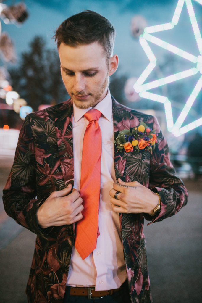 Groom buttoning his suit lit by neon lights at the fair