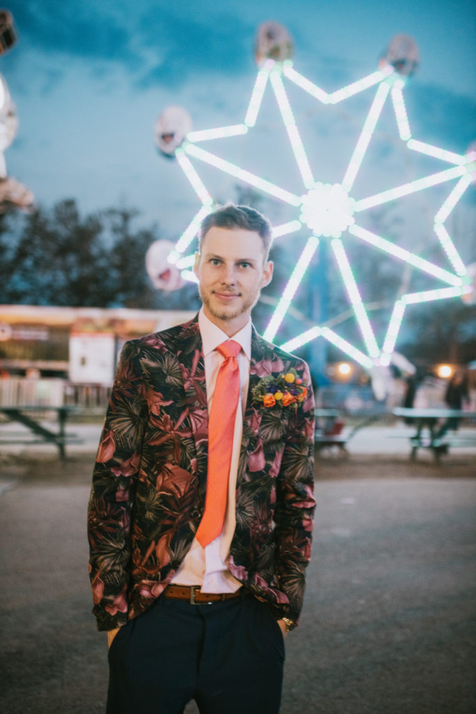 Groom smiling in front of a lit up ferris wheel