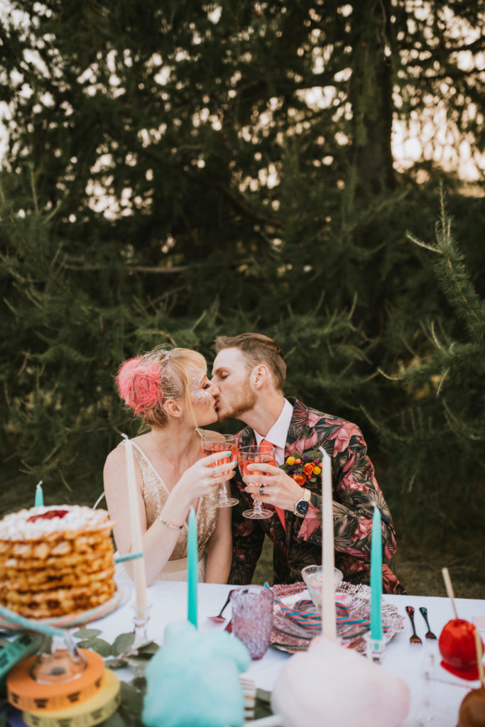 Colorful bride and groom kissing while cheersing their cotton candy cocktails