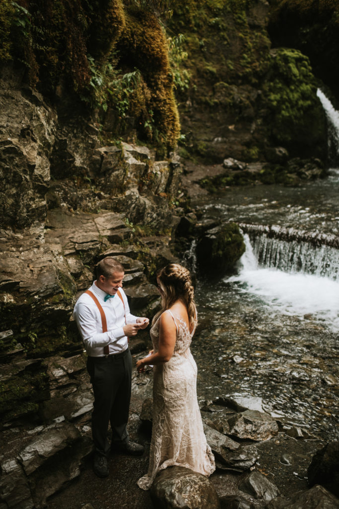 Couple standing at base of waterfall reading each other their vows