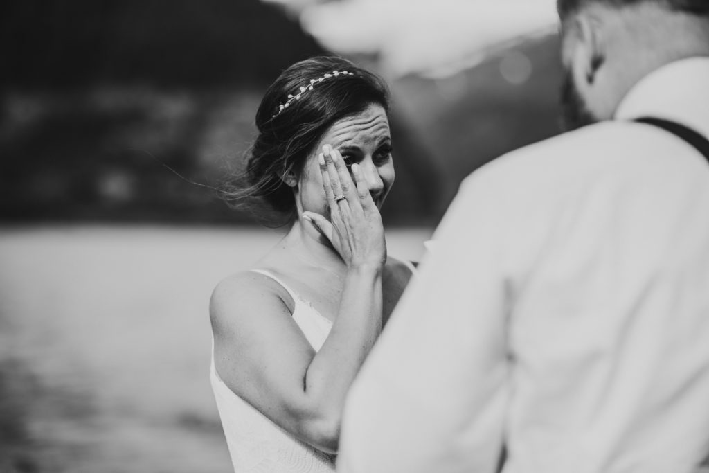 black and white photo of bride wiping tears away while listening to vows