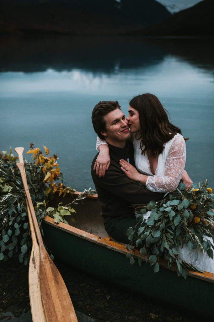 Bride kissing a grooms cheek in a canoe on a lake