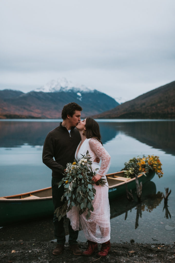 Couple kissing on Eklutna Lake Lakeshore with canoe and mountains in the background