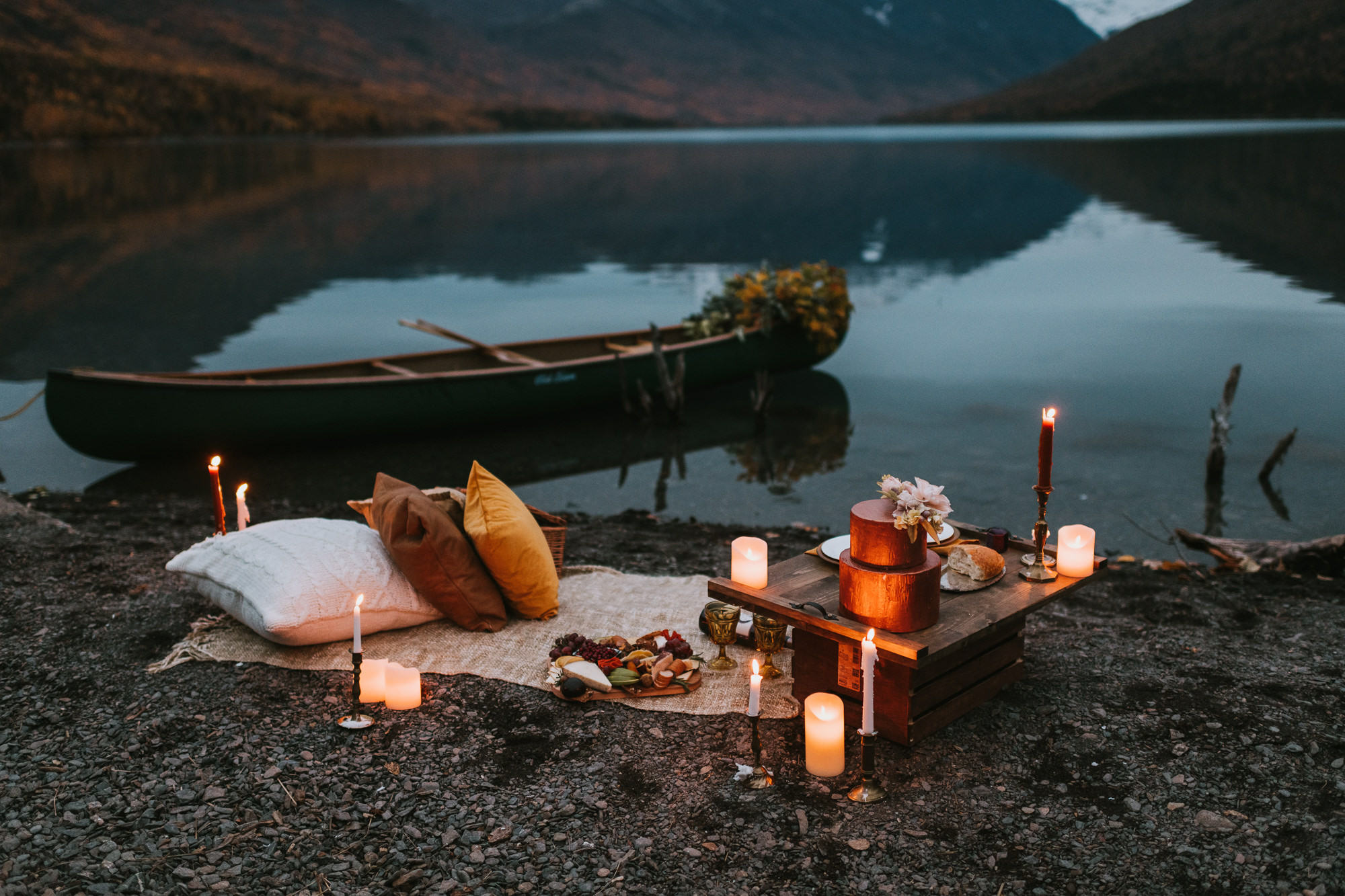 Romantic candlelit picnic on lakeshore with canoe and florals