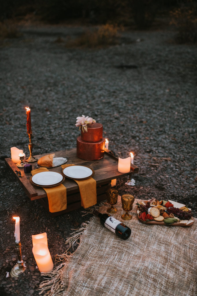 Candlelit elopement picnic on a lake shore with charcuterie wine and cake