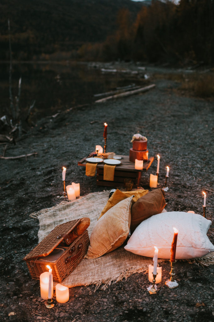 Romantic candlelit picnic on lake shore with food and drinks