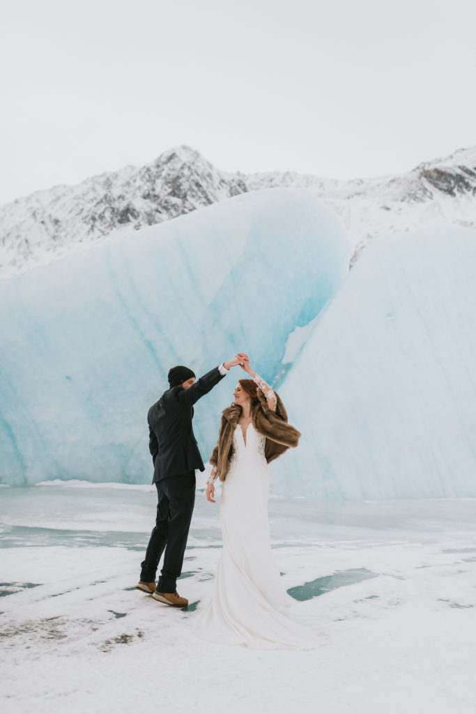 groom twirling his bride in front of a blue iceburg