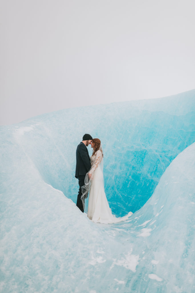 Bride and groom standing facing each other on a blue iceburg