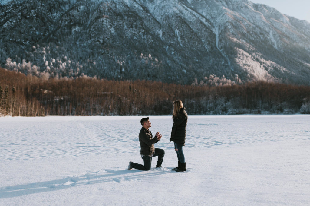 man kneeling on frozen lake proposing to his girlfriend