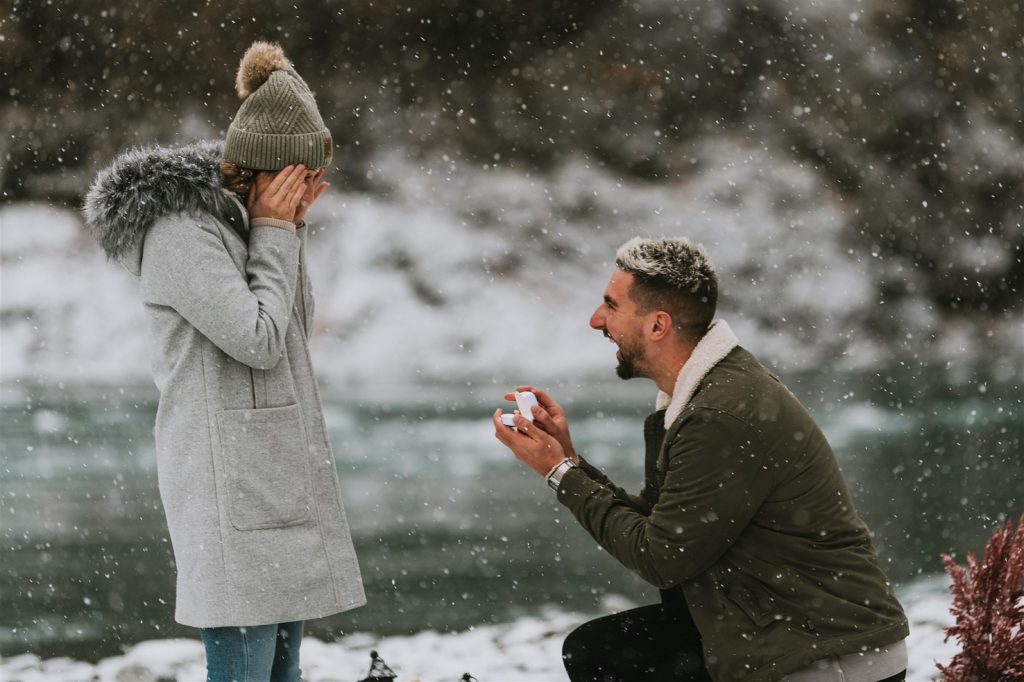 Surprised partner smiling during a heartfelt marriage proposal in Alaska outdoors with a scenic, natural backdrop, capturing the moment of engagement