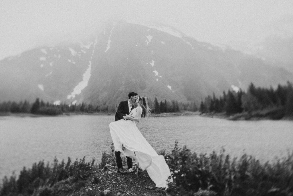 couple dip kissing on the lake shore against a mountain backdrop