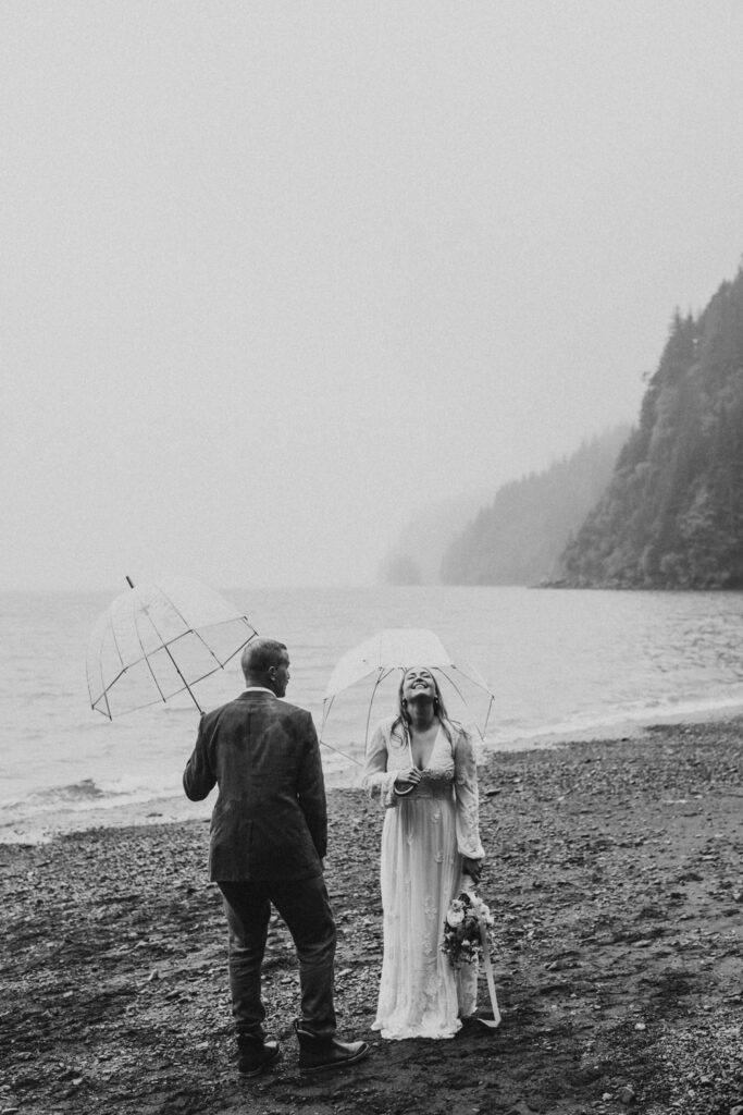 black and white image couple laughing in the rain on a beach in seward alaska for their wedding