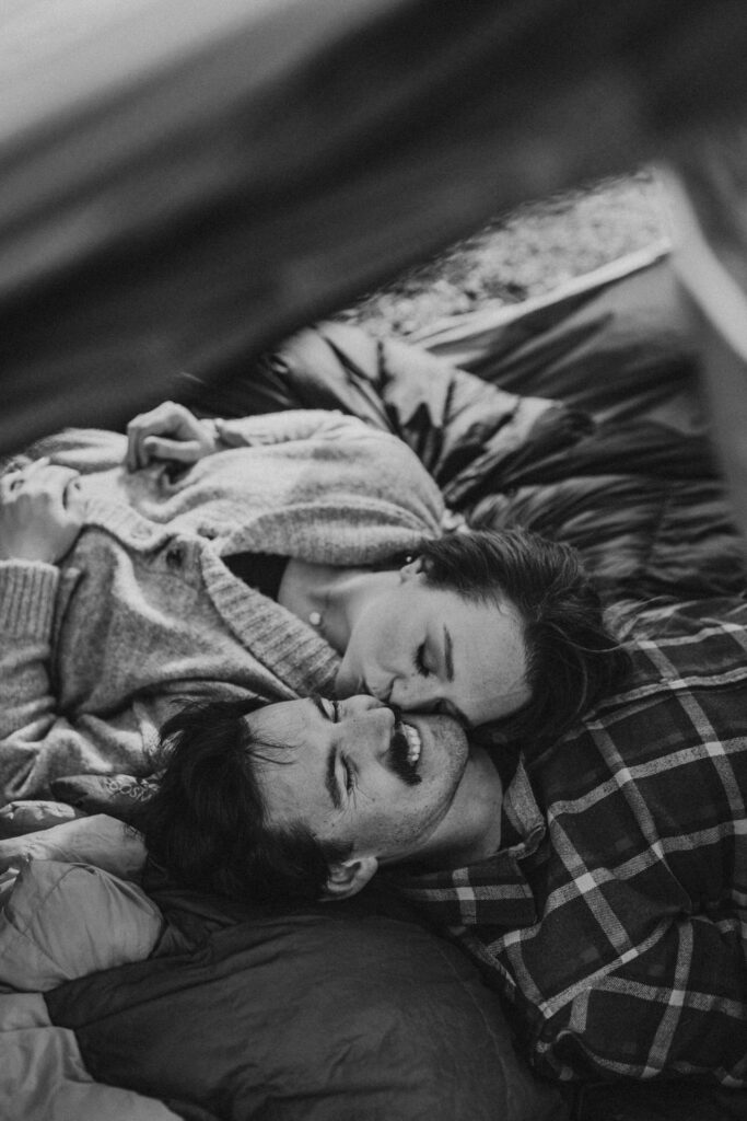 couple laying inside of a tent while she kisses him on the cheek