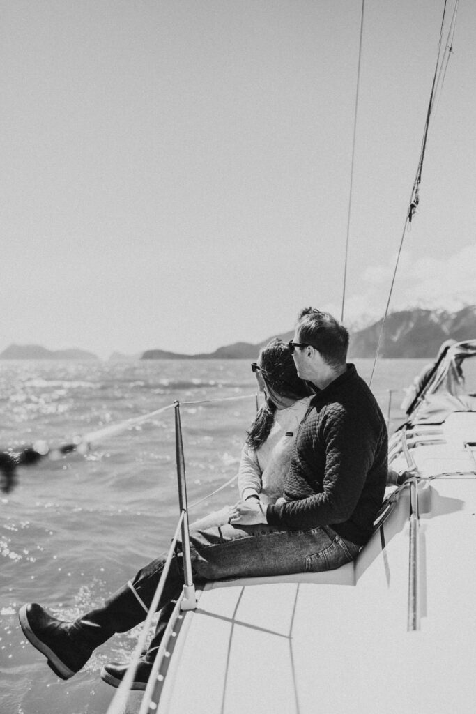 couple sitting on the side of a sailboat enjoying the mountain views