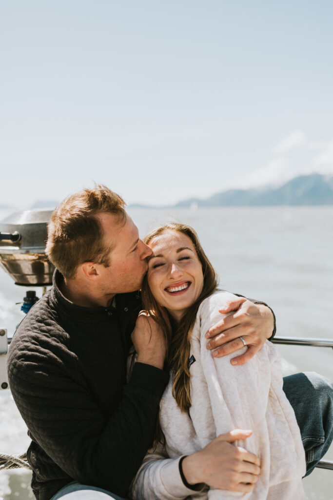 couple snuggling on a sailboat with mountain backdrops
