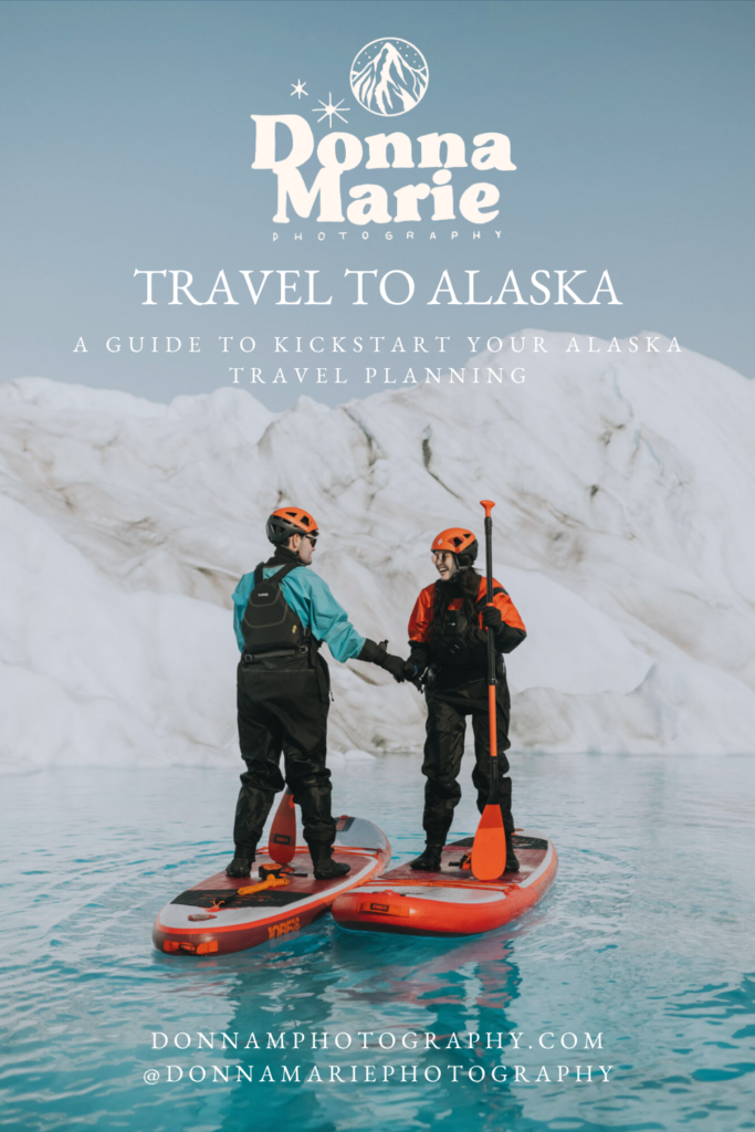 Two people in outdoor gear stand on paddleboards, shaking hands on calm water with a snowy mountain backdrop. Text promotes an Alaska travel guide by Donna Marie Photography, highlighting the best time to travel to Alaska for adventure.