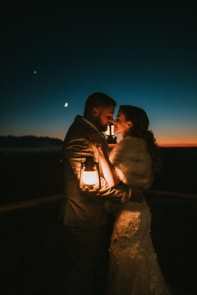 A couple embraces, their love glowing like a lantern against the twilight sky, as a crescent moon and stars witness their winter elopement.