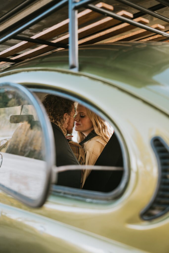 Two people sitting close together in an old green car, viewed through the rear window.