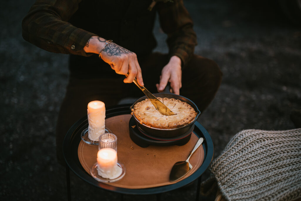 A person cuts a pie beside two lit candles on a round table.