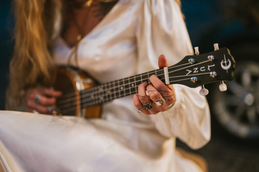 A person in a white dress plays a string instrument with decorated hands.