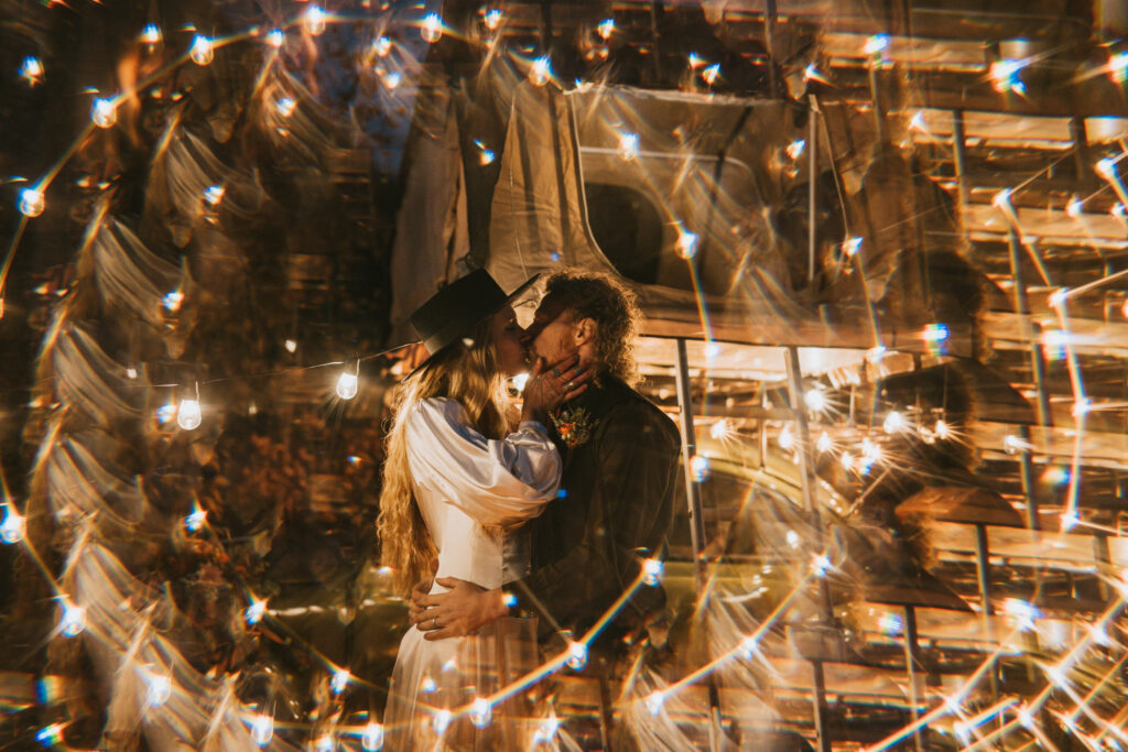 A couple kisses surrounded by strings of glowing lights, creating a dreamy, circular blur effect in the foreground.