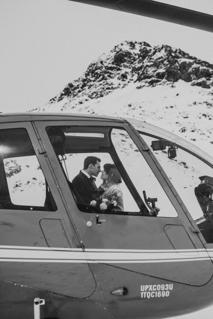 A couple inside a helicopter are about to kiss, their hearts as high as the snow-covered mountains in the background.