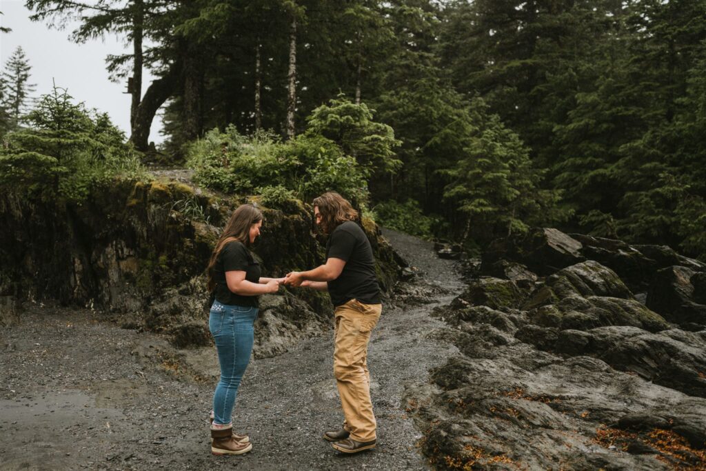 Two people stand facing each other, holding hands on a rocky outdoor path surrounded by dense green trees—an intimate setting perfect for unique proposal ideas.