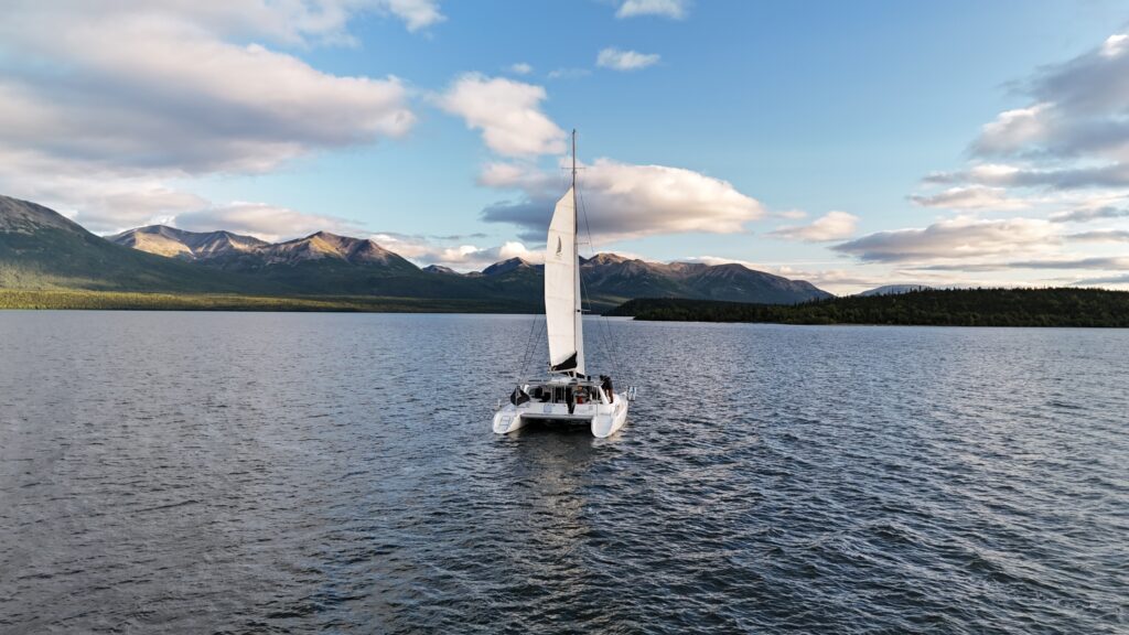 A white catamaran sails on a calm lake surrounded by mountains and partially cloudy skies—an idyllic setting perfect for romantic proposal ideas.