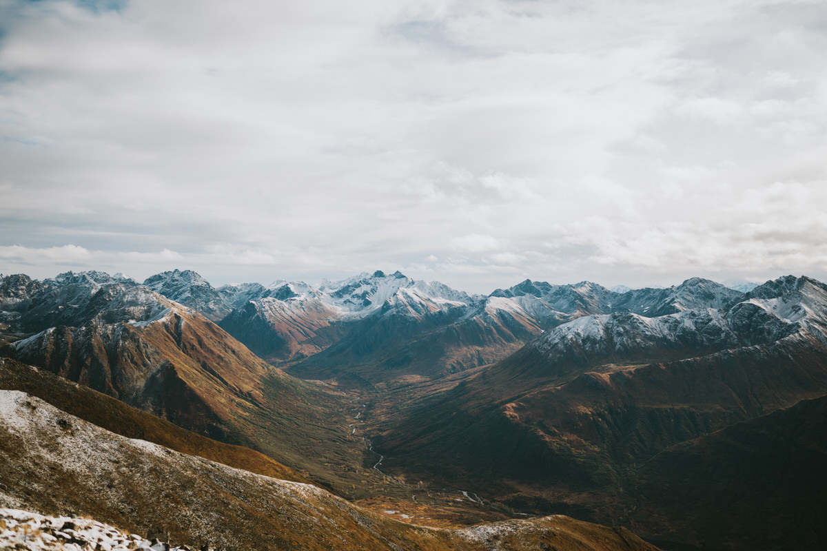 Snow-capped mountains and a wide valley under a cloudy sky, with a river winding through the landscape—perfect scenery for alaska hikes.