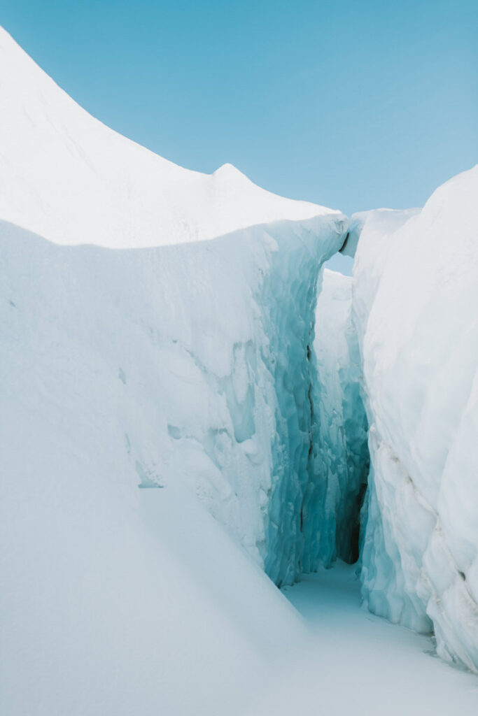 Snow-covered icy crevasse with high walls under a clear blue sky, reminiscent of spectacular Alaska hikes.